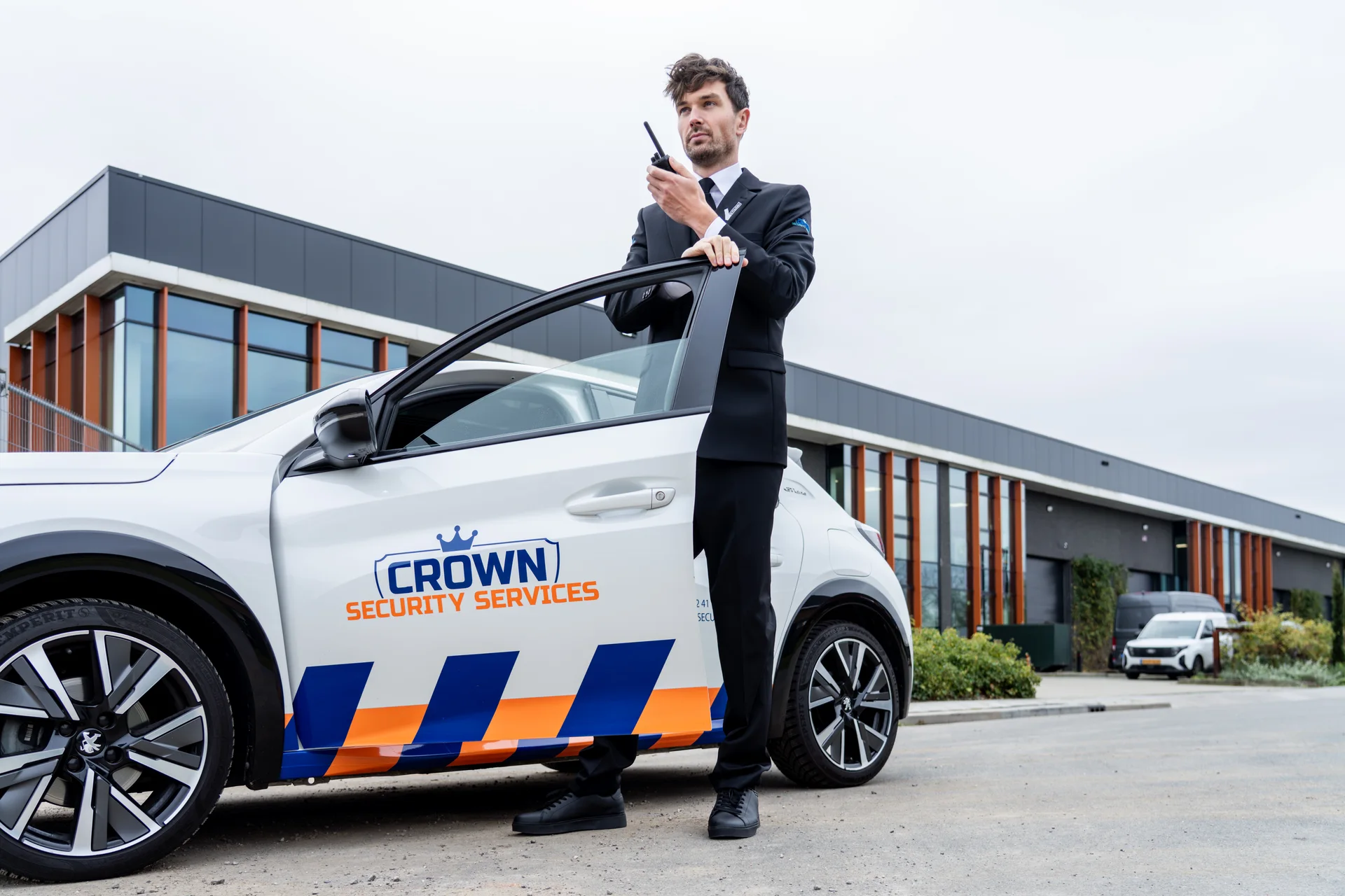 Crown-beveiliger met portofoon bij een Crown-dienstvoertuig